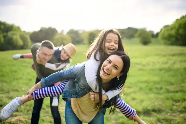 Happy family with two small daughters having fun outdoors in spring nature, giving piggyback ride.