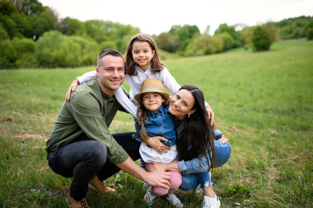 istock Happy family with two small daughters sitting outdoors in spring nature, looking at camera. 1250032164