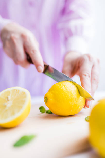 istock Female hands slicing lemon on half with knife on cutting board. 1250033050