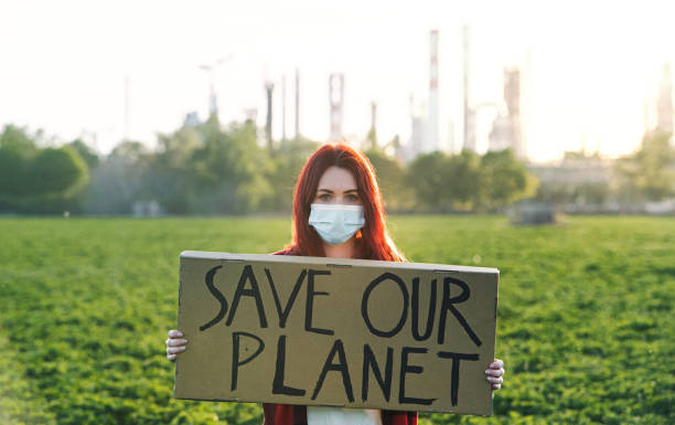 istock Young woman activist with placard standing outdoors by oil refinery, protesting. 1250034120