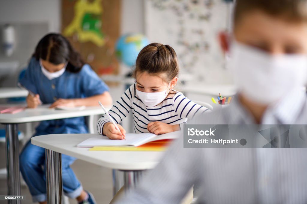 Children with face mask back at school after covid-19 quarantine and lockdown. Small children with face mask back at school after covid-19 quarantine and lockdown, writing. School Building Stock Photo