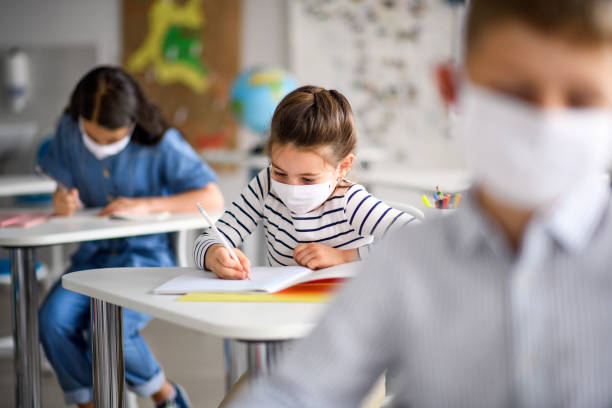 Children with face mask back at school after covid-19 quarantine and lockdown. Small children with face mask back at school after covid-19 quarantine and lockdown, writing. school building stock pictures, royalty-free photos & images