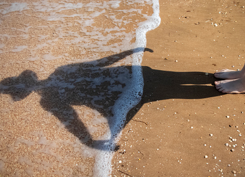 Shadow and reflection of a woman's dress on a sunny beach. The concept of lifestyle, rest and relaxation on the sea or the ocean. Girl on a background of the sea.