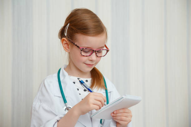 istock Little girl in a doctor s coat smiles and makes notes in a notebook. 1250041964