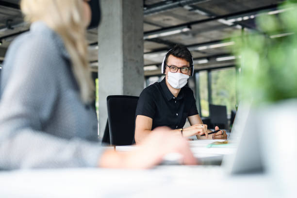 istock Young people with face masks back at work in office after lockdown, talking. 1250042616