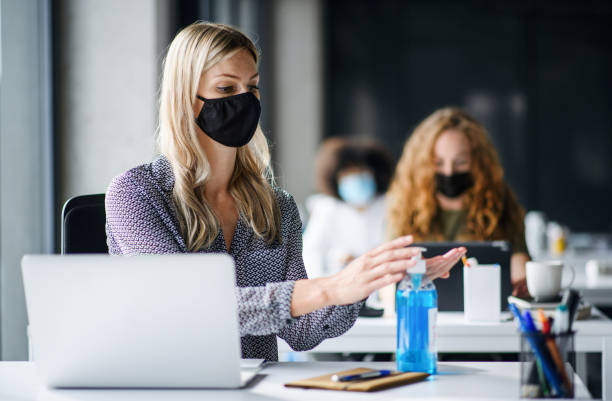 istock Young woman with face mask back at work in office after lockdown, disinfecting hands. 1250042749