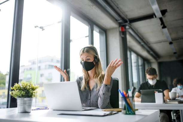 istock Young woman with face mask back at work in office after lockdown, having video call. 1250042815