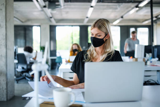 istock Young woman with face mask back at work in office after lockdown, working. 1250042835