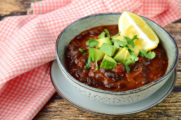 Hausgemachte vegane schwarze Bohnen-Chili-Tomatensuppe mit gewürfelter Avocado und gehackter Petersilie mit Zitrone – Foto