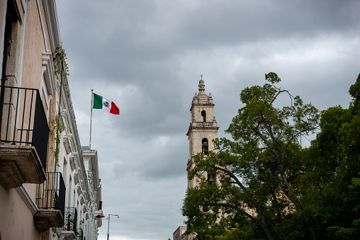 The flag of Mexico flies from the top of a building in Merida, Yucatan, Mexico. The city's cathedral is on the right.