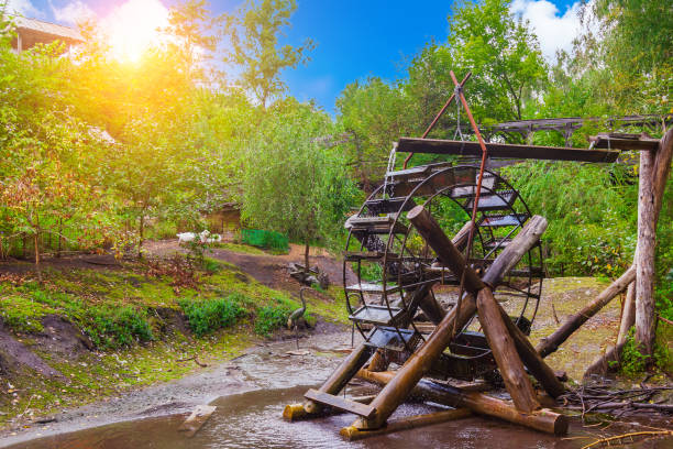 An old wooden water mill made by yourself from large logs stands on a stream against a blue sky in the sun in the Altai Valley. Agriculture in Russia is a cozy courtyard with geese.