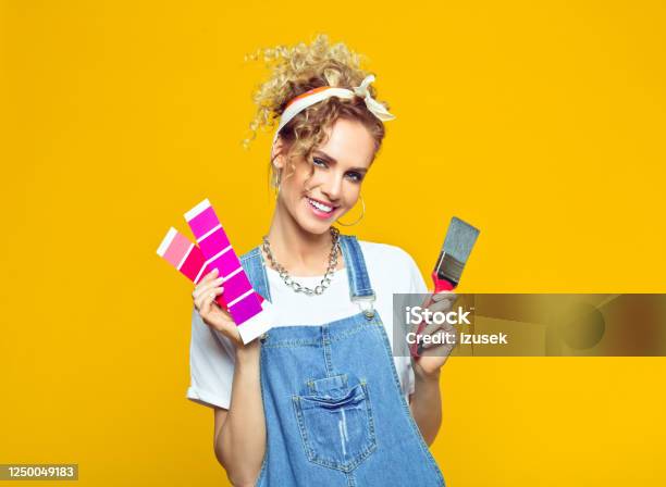 Young Woman In Coveralls Holding Color Swatch And Paintbrush Stock Photo - Download Image Now