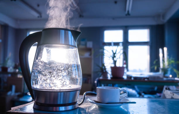 Transparent kettle with water boils A transparent kettle of water boils against the background of the sunset shining through the window. The concept of coffee break and end of the working day. glass cup of boiling water stock pictures, royalty-free photos & images