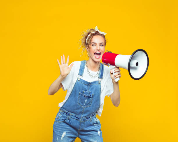 Young woman in dungarees shouting into megaphone