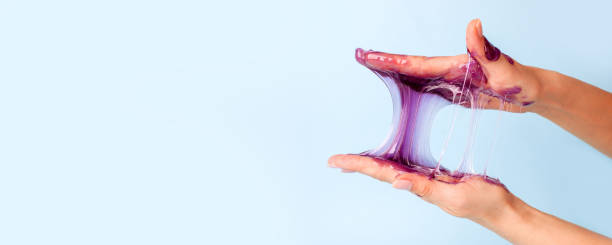 Young girl hands with sticky purple slime on blue background, liquid wax for depilation, conceptual flyer banner with copy space, antistress relax, modern kids hobby oddly satisfying semi surreal asmr manos de niña joven con baba púrpura pegajosa sobre fondo azul, cera líquida para la depilación, banner de volante conceptual con espacio de copia, antiestresa relajarse, pasatiempo de los niños modernos extrañamente satisfactorio semi surrealista as