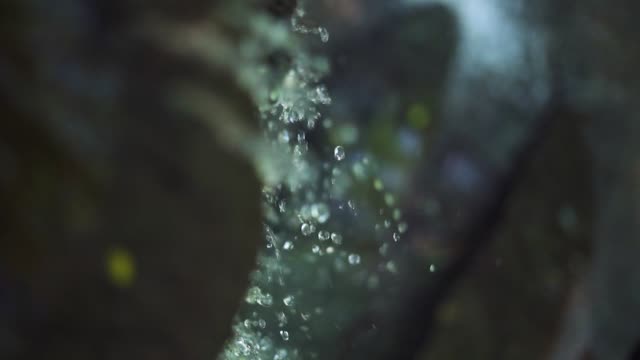 Water droplets and spray flowing and splashing on rock at waterfall. Close up