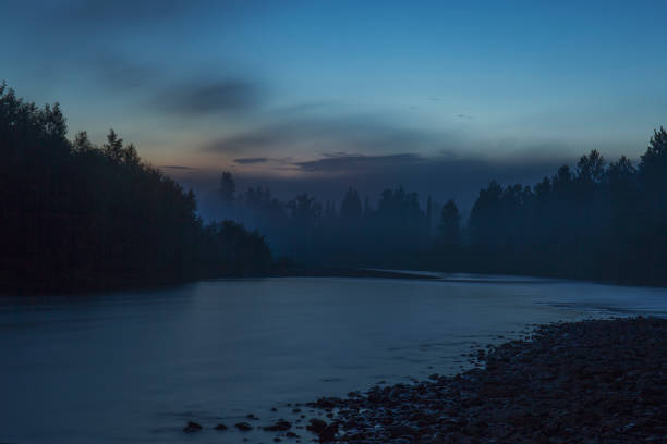 Night landscape: a small flat river, a dense coniferous forest and a pink sunset with clouds. Photos from a trip to Russia in the summer.