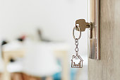 Key with keychain in a house shape and family in the door keyhole. Buy new home concept. Opened door to a new house.