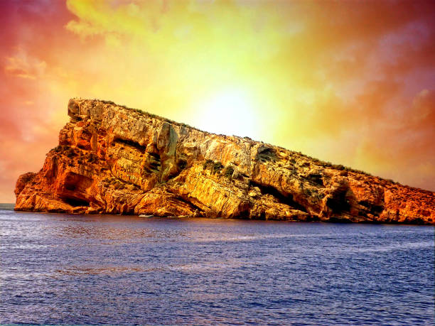 Benidorm Island off the coast of Valencia, Spain. The photograph was taken in summer taking advantage of the sunrise light creating a wide range of colors over the sky. The island of Benidorm or islet of Benidorm, also known as the island of journalists, is a small island located off the coast of Benidorm. It has a high ecological, landscape and environmental interest. It is located about two nautical miles from the port of Benidorm.
