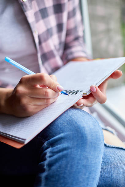 Woman, sitting at window at home, writes in notebook goals