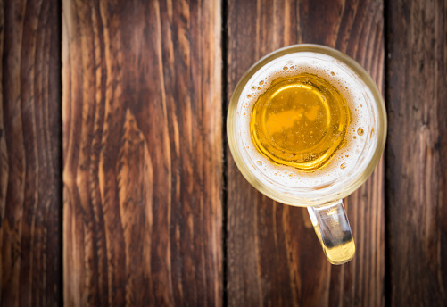 A refreshing pint of cold beer on a wood surface with white background.