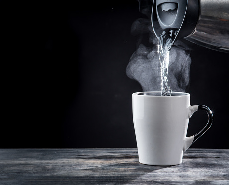Pouring hot water into into a cup on a black background