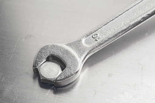 Wrench tightens  bolt in steel billet. Spanner, bolt, screw and nuts.