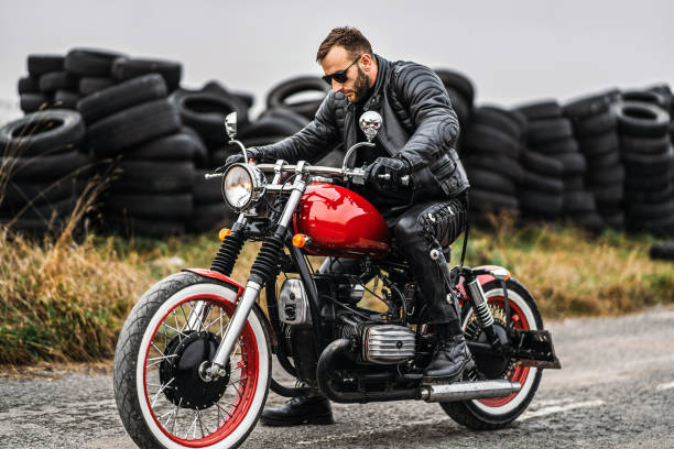 Red motorbike with rider. A man in a black leather jacket and pants starts a motorcycle. Tires are laid on the background stock photo