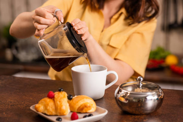 istock Young female sitting by table in the kitchen and pouring black tea into cup 1250074239