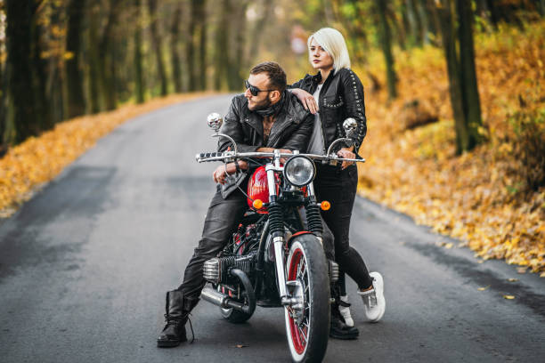 Pretty couple near red motorcycle on the road in the forest with colorful blured background stock photo
