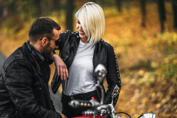 Pretty couple near red motorcycle on the road in the forest with colorful blured background stock photo