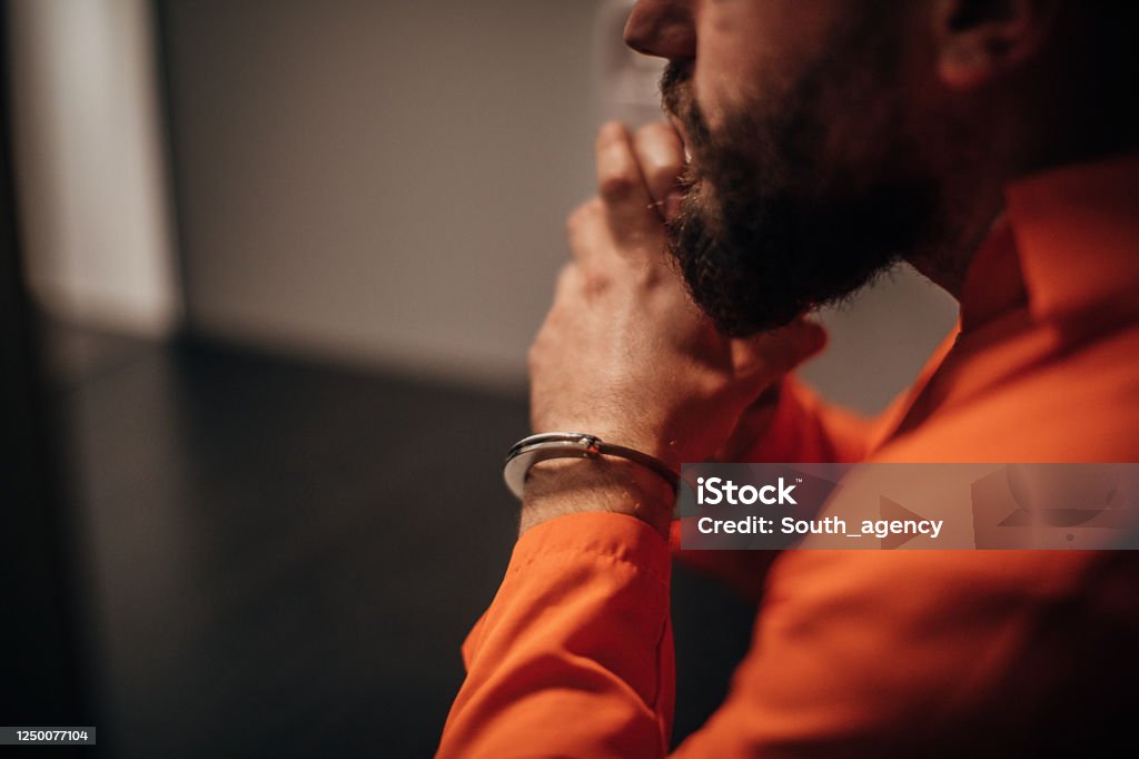Prisoner in orange jumpsuit sitting in prison visiting room One mal prisoner in orange jumpsuit sitting in prison visiting room. Prisoner Stock Photo