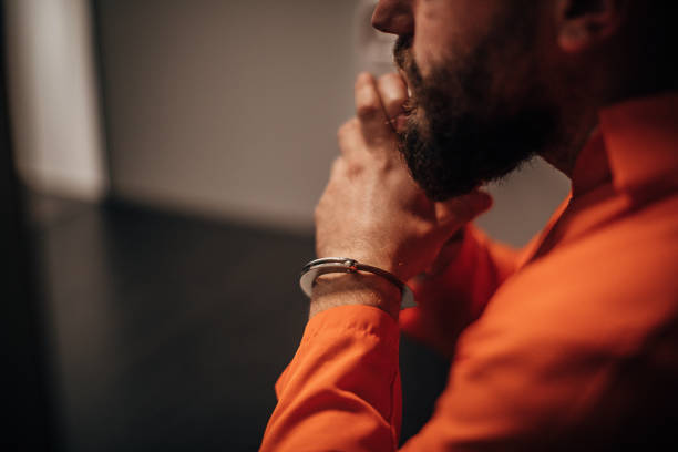 Prisoner in orange jumpsuit sitting in prison visiting room One mal prisoner in orange jumpsuit sitting in prison visiting room. murderer stock pictures, royalty-free photos & images