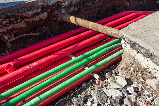 A large number of modern plastic cable protection pipes for electricity cabling (in the red pipe ducts) and fibre optic (green), during an installation in a trench dug in the street.