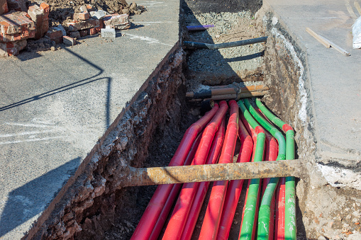 A large number of modern plastic cable protection pipes for electricity cabling (in the red pipe ducts) and fibre optic (green), during an installation in a trench dug in the street.
