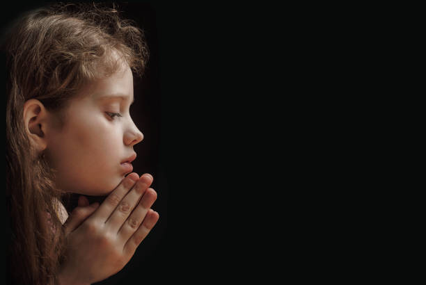 Beautiful little girl in communion dress with eyes closed and hands together praying.