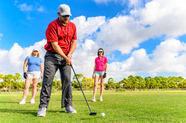 trio joue au golf sur un beau vert scénique, homme et deux femmes sportives - golf golf swing putting cheerful photos et images de collection