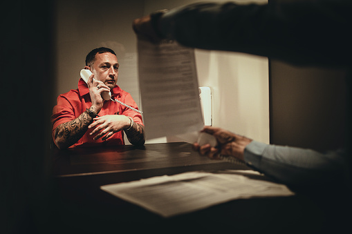 One male detective interrogating a prisoner in prison visiting room.