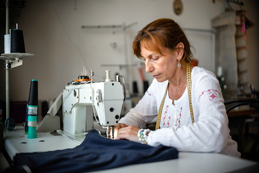 Woman sewing on sewing machine in small studio, fashion atelier, slow fashion, tailor craft, handmade clothes