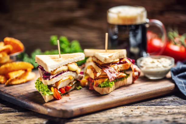 Chicken and cheese sandwich with bacon, red cabbage, peppers and salad with a dark beer in the background Chicken and cheese sandwich with bacon, red cabbage, peppers and salad with a dark beer in the background. sandwich club sandwich lunch restaurant stock pictures, royalty-free photos & images