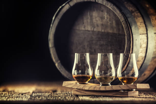 tazas de degustación de whisky glencairn sobre una porción de madera, con un barril de whisky en el fondo oscuro - whisky escocés fotografías e imágenes de stock