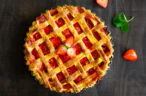 Pie with rhubarb and strawberries on a dark wooden background with fresh strawberries. Horizontal orientation, top view