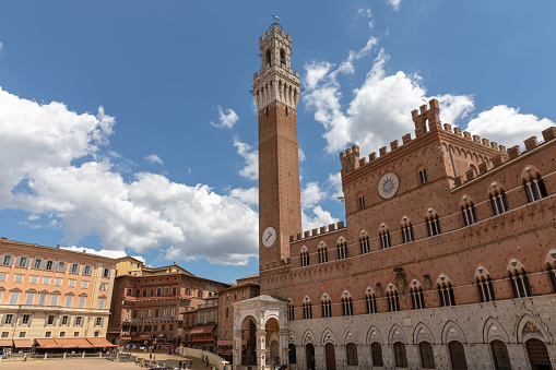 Siena, Italy - June 28, 2018: Panoramic view of Palazzo Pubblico (town hall) is a palace and Torre del Mangia is a tower in city on Piazza del Campo. Summer sunny day and dramatic blue sky
