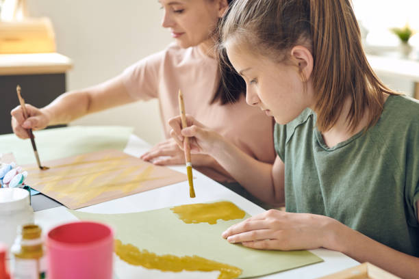 Using paints while making picture Concentrated teenage daughter sitting at table and using paints while making picture with mother art class photos stock pictures, royalty-free photos & images