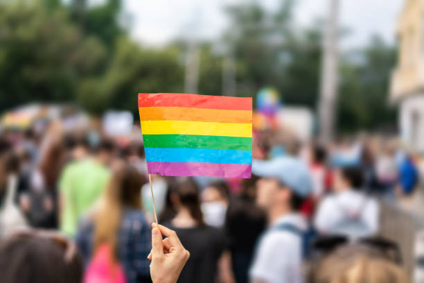 homosexuell regenbogen-flagge bei homosexuell stolz parade mit verschwommenen teilnehmern im hintergrund - pride lgbtqi veranstaltung stock-fotos und bilder