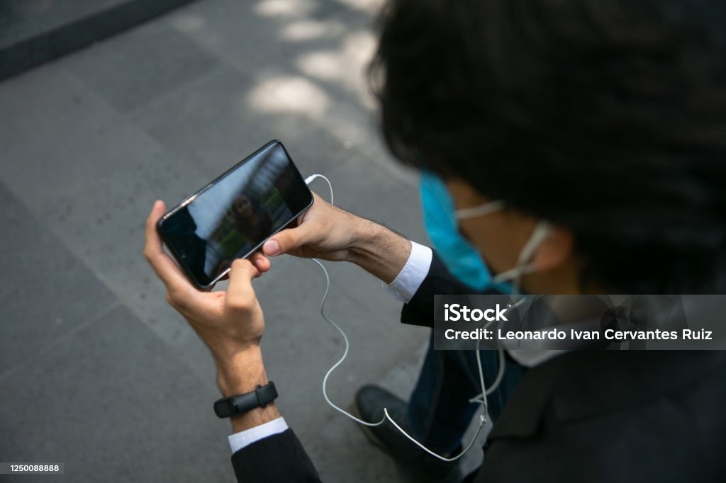 Men Covering His Face With Protective Mask Stock photo of men using mobile phone in the street. "r"nHe has headphones. He is wearing a protective mask for the prevention of a virus. Coronavirus concept Healthcare And Medicine Stock Photo