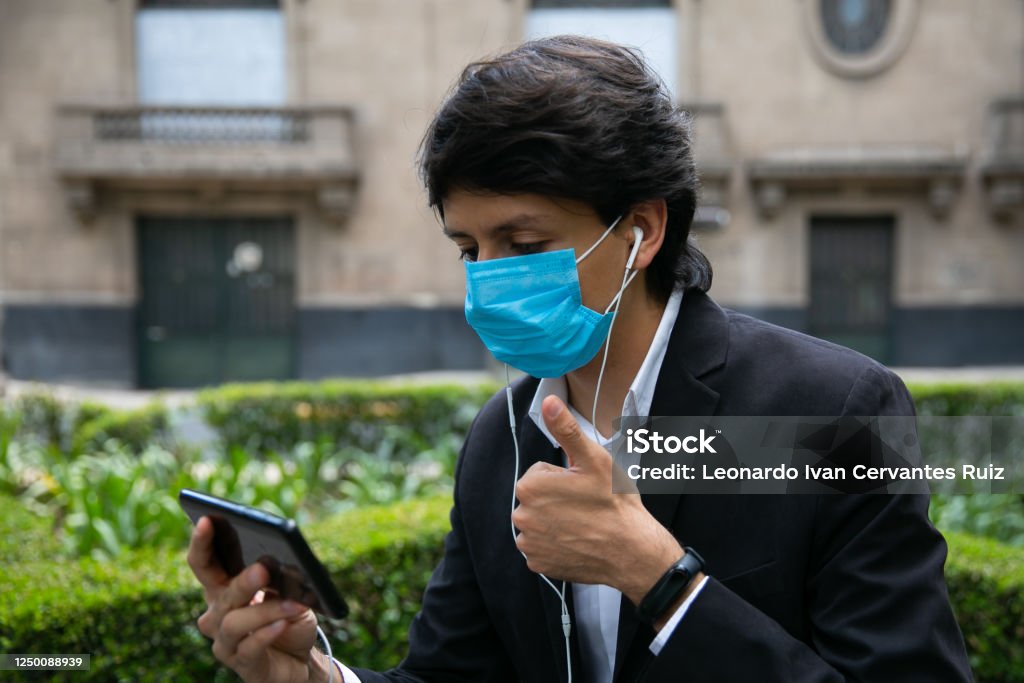 Men Covering His Face With Protective Mask Stock photo of men using mobile phone in the street. He is wearing a protective mask for the prevention of a virus. Coronavirus concept Adult Stock Photo