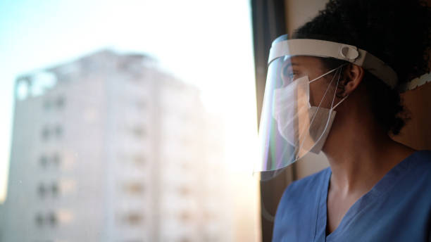 krankenschwester mit schützender gesichtsmaske, die durch das fenster im krankenhaus schaut - behind glass concept hope stock-fotos und bilder