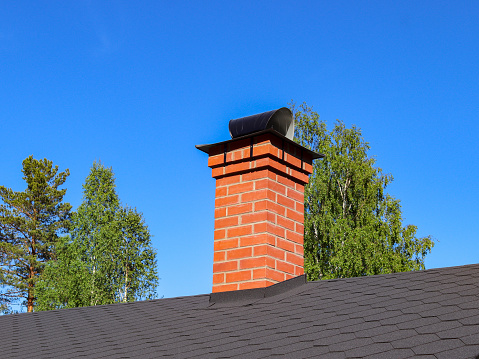 Red brick chimney on black roof of a newly built house
