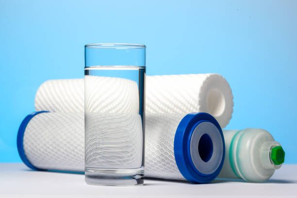 A glass of drinking water and filter cartridges A glass of drinking water and filter cartridges to domestic water treatment systems at bright blue background. Concept of water treatment technology bullet cartridge photos stock pictures, royalty-free photos & images